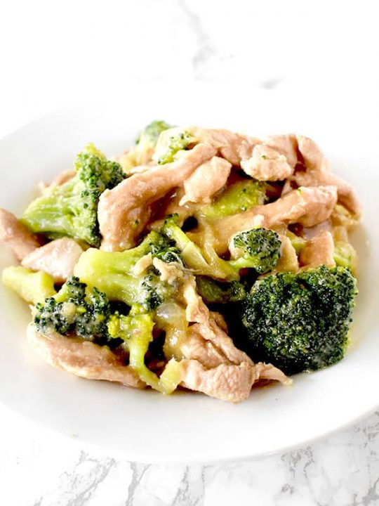 Chicken and broccoli on a white plate on a white marble counter