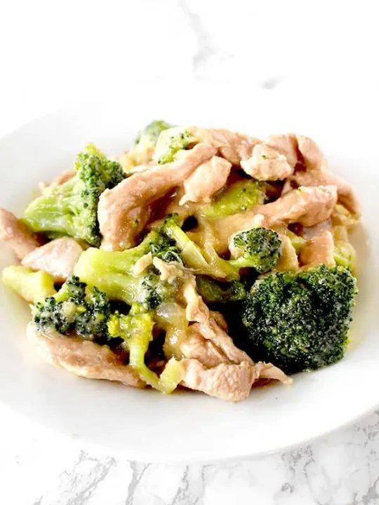 Chicken and broccoli on a white plate on a white marble counter