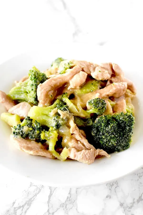 Chicken and broccoli on a white plate on a white marble counter