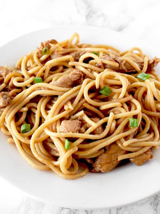 Chicken lo mein on a whit plate on a white marble counter