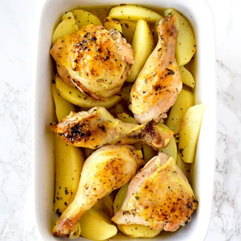 Greek lemon chicken and potatoes in a ceramic pan on a white marble counter