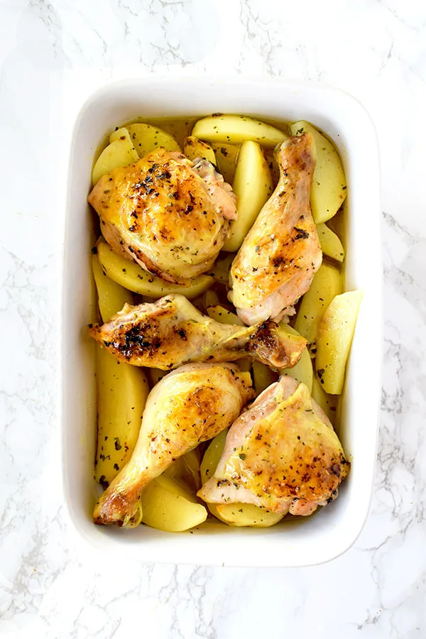 Greek lemon chicken and potatoes in a ceramic pan on a white marble counter