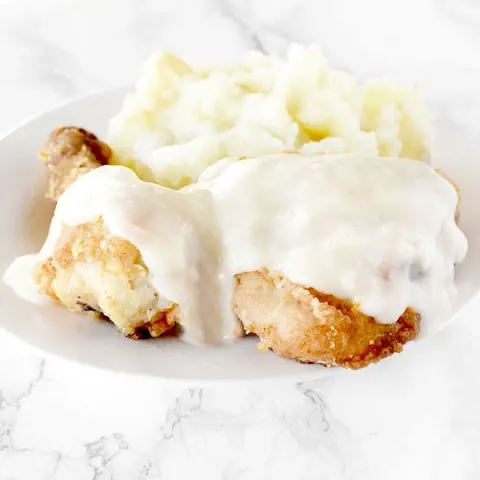 Maryland fried chicken with mashed potatoes on a white plate on a white marble counter