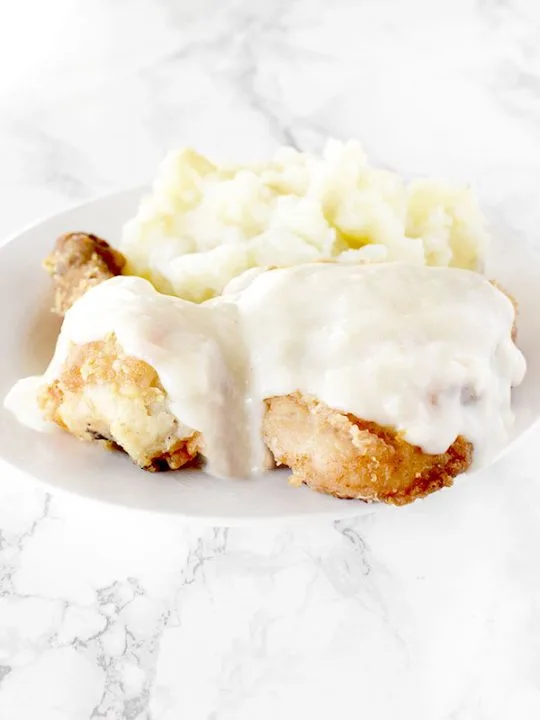 Maryland fried chicken with mashed potatoes on a white plate on a white marble counter