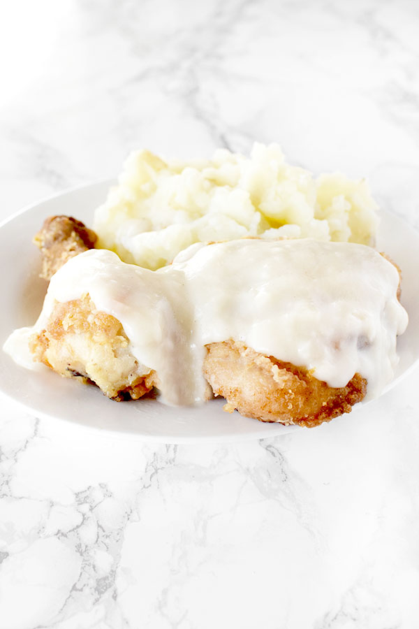 Maryland fried chicken with mashed potatoes on a white plate on a white marble counter