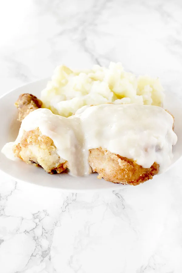 Maryland fried chicken with mashed potatoes on a white plate on a white marble counter