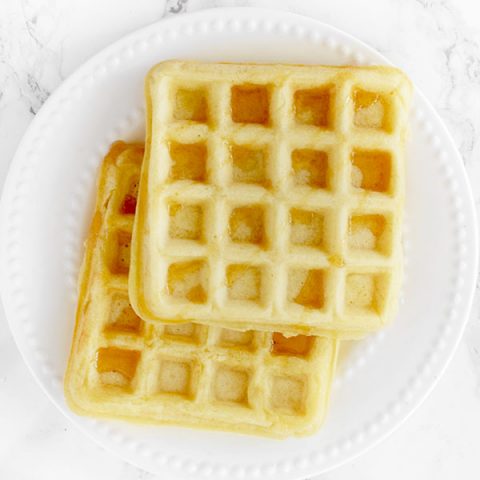 two waffles stacked on a white plate on a white marble counter