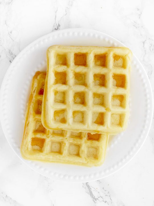 two waffles stacked on a white plate on a white marble counter