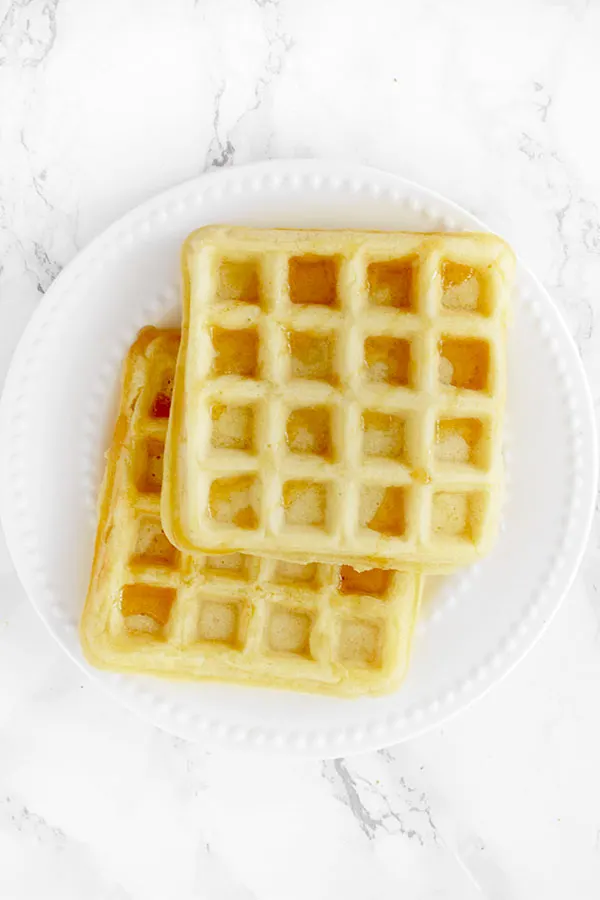 two waffles stacked on a white plate on a white marble counter
