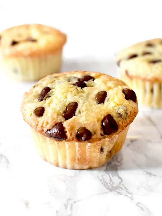 three chocolate chip muffins with oil on a marble counter