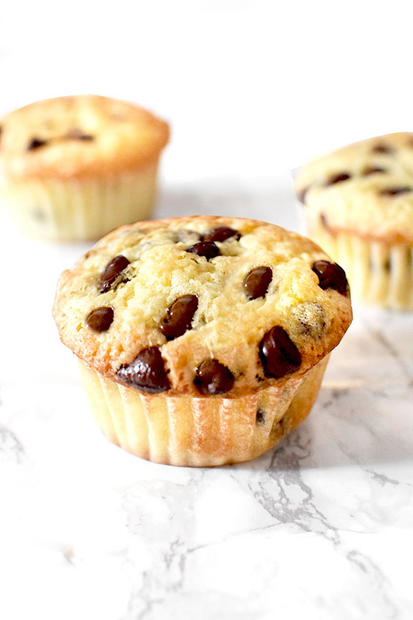 three chocolate chip muffins with oil on a marble counter