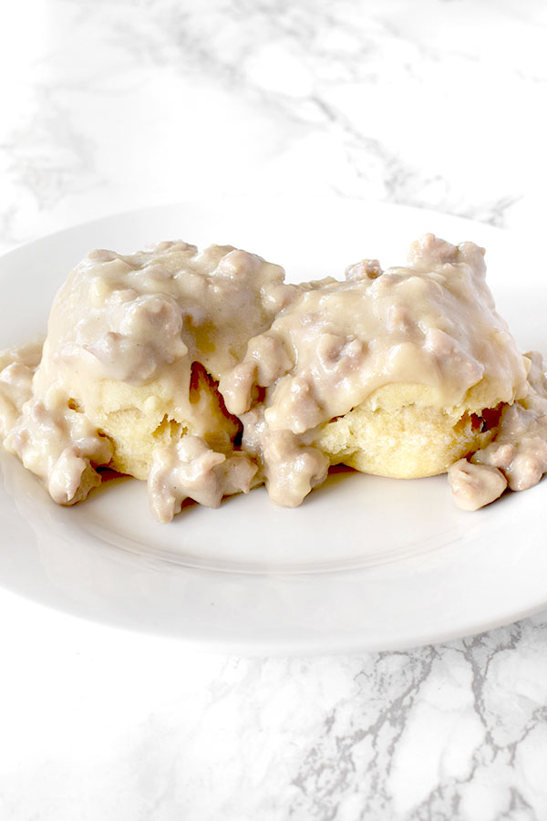 Biscuits and gravy with oat milk on a white plate on a white marble counter