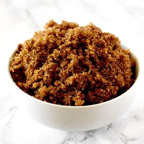 Dark brown sugar in a white bowl on a white marble counter