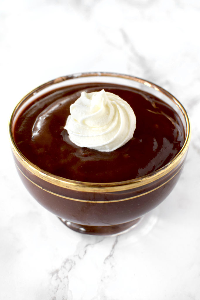 Chocolate pudding in oat milk in a glass bowl on a white marble counter