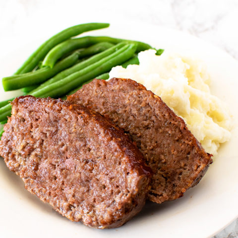 Meatloaf with green beans and mashed potatoes on a white plate on a white marble counter