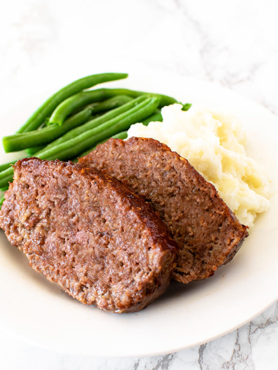 Meatloaf with green beans and mashed potatoes on a white plate on a white marble counter