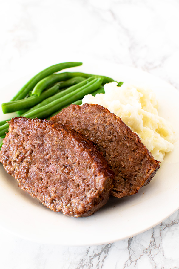 Meatloaf with green beans and mashed potatoes on a white plate on a white marble counter