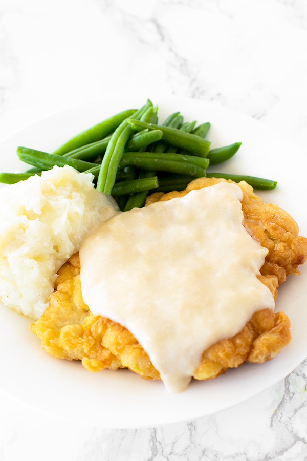 Chicken fried chicken with mashed potatoes and green beans on a white plate on a  white marble counter