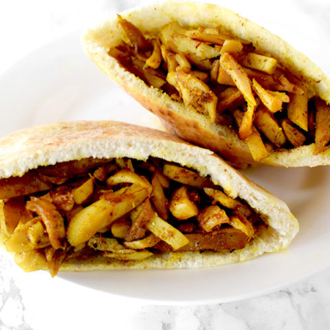 Two shawarma filled pitas on a white plate on a white marble counter