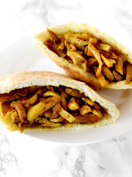 Two shawarma filled pitas on a white plate on a white marble counter