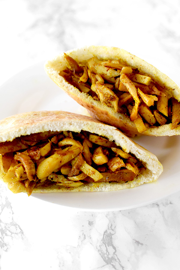 Two shawarma filled pitas on a white plate on a white marble counter