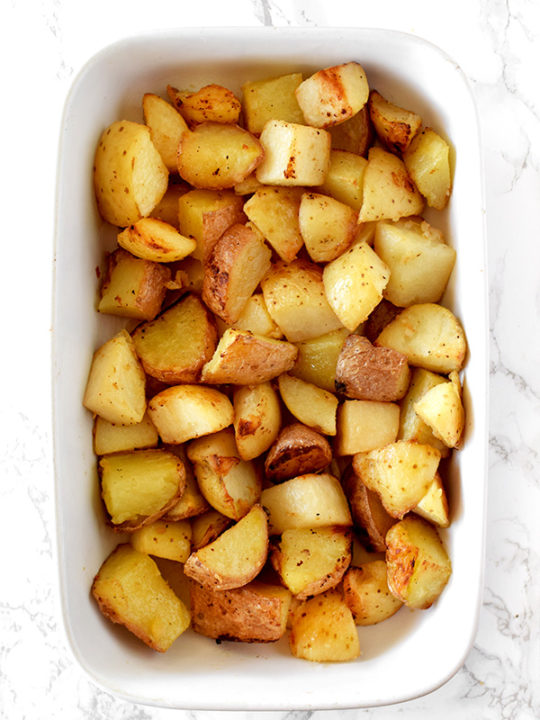 garlic roasted potatoes in a white casserole dish on a white marble counter