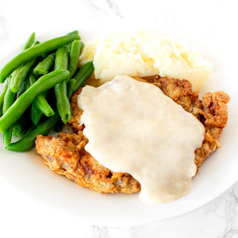 Chicken fried steak on a white plate on a white marble counter