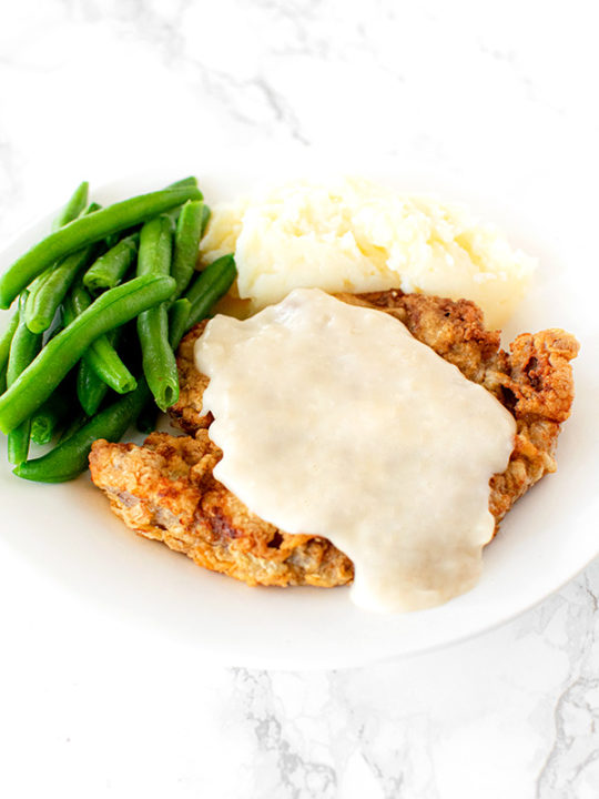 Chicken fried steak on a white plate on a white marble counter