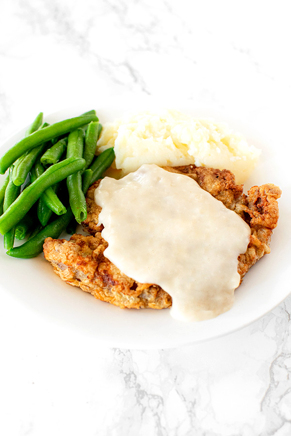 Chicken fried steak on a white plate on a white marble counter