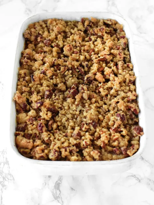 sweet potato casserole with pecans in a white casserole dish on a white marble counter