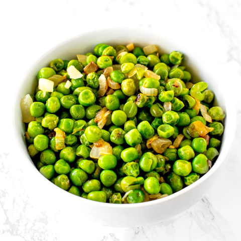 sauteed peas with onions on a white plate on a white marble counter