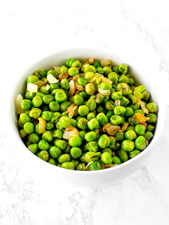 sauteed peas with onions on a white plate on a white marble counter