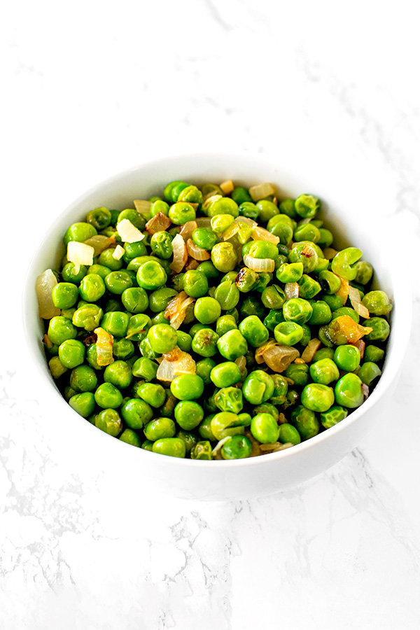 sauteed peas with onions on a white plate on a white marble counter