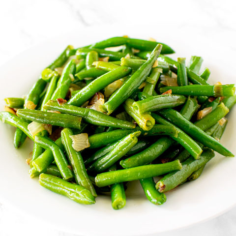 sauteed green beans with onions on a white plate on a white marble counter