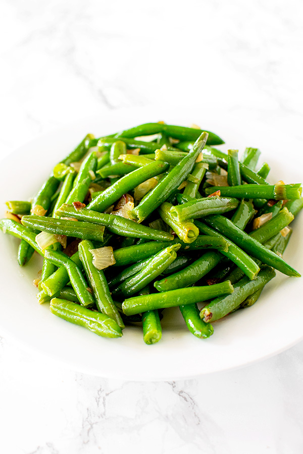 sauteed green beans with onions on a white plate on a white marble counter