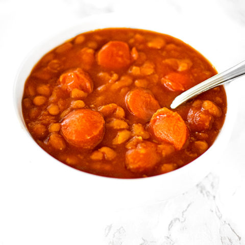 Franks and beans in a white bowl on a white marble counter