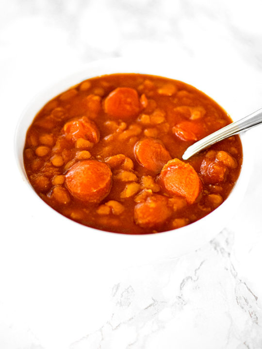 Franks and beans in a white bowl on a white marble counter