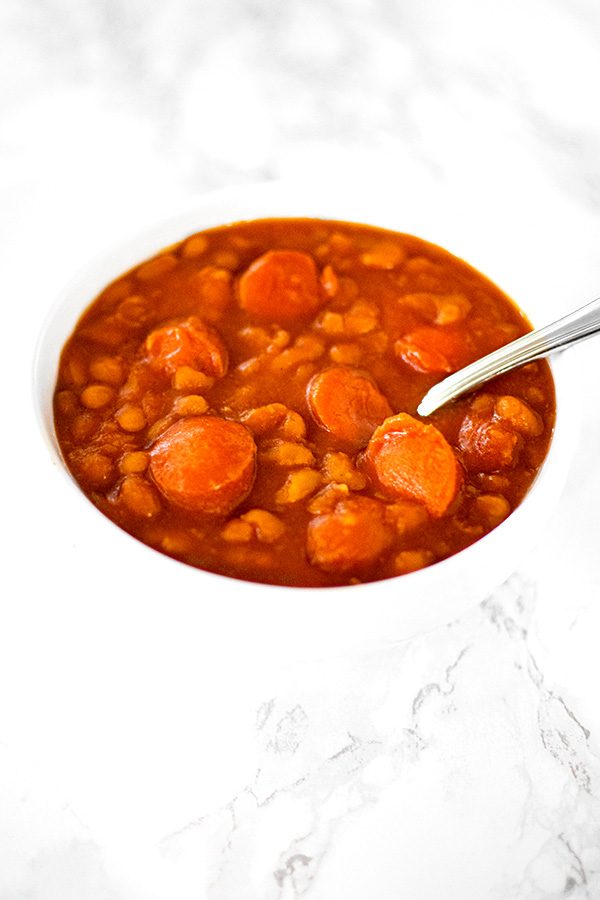 Franks and beans in a white bowl on a white marble counter