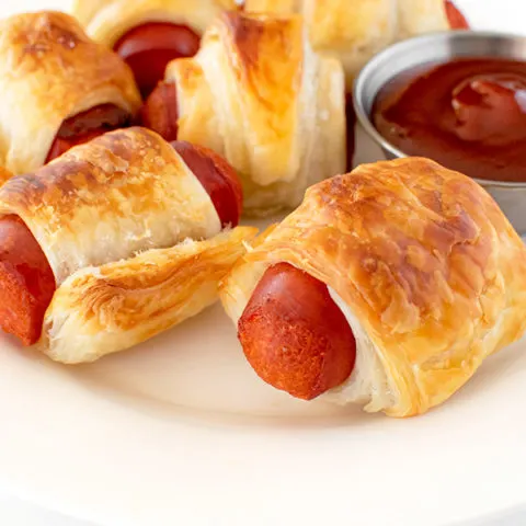 Franks in a blanket on a white plate on a white marble counter