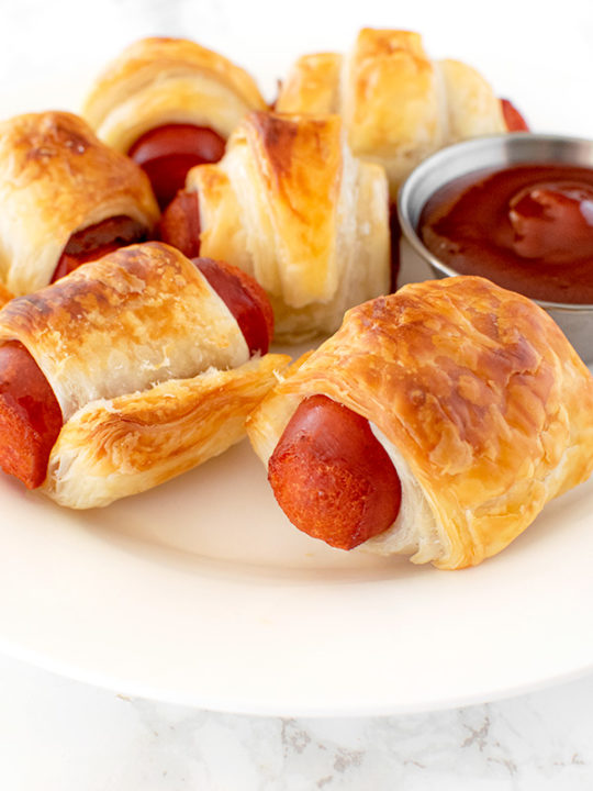 Franks in a blanket on a white plate on a white marble counter