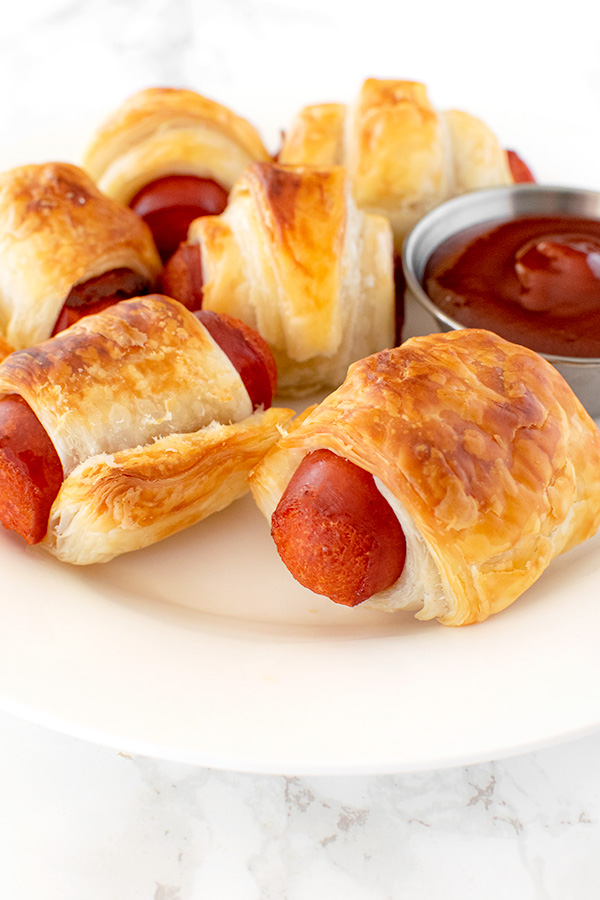 Franks in a blanket on a white plate on a white marble counter