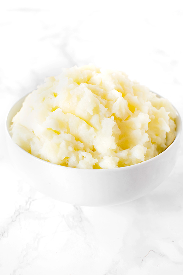 mashed potatoes without butter in a white bowl on a white marble counter