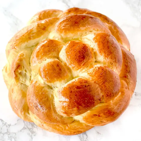 Round honey challah on a white marble counter