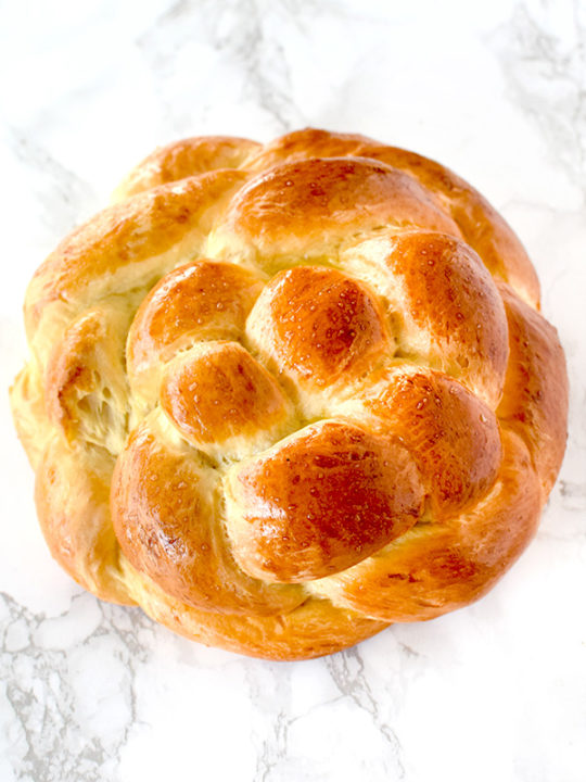 Round honey challah on a white marble counter