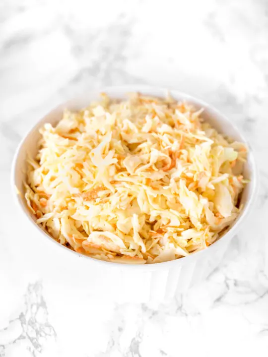 dairy free coleslaw in a white bowl on a white marble counter