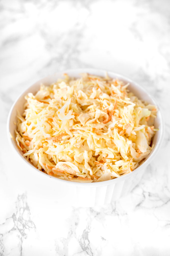 dairy free coleslaw in a white bowl on a white marble counter