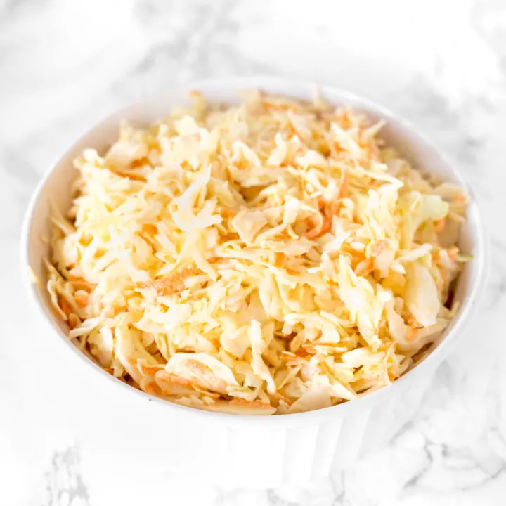 dairy free coleslaw in a white bowl on a white marble counter