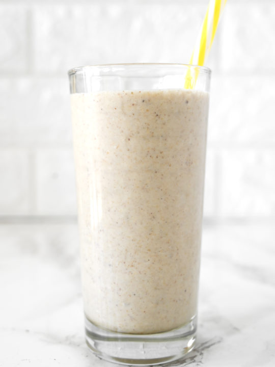 Banana Smoothie with Almond Milk in a glass on a white marble counter with a yellow straw