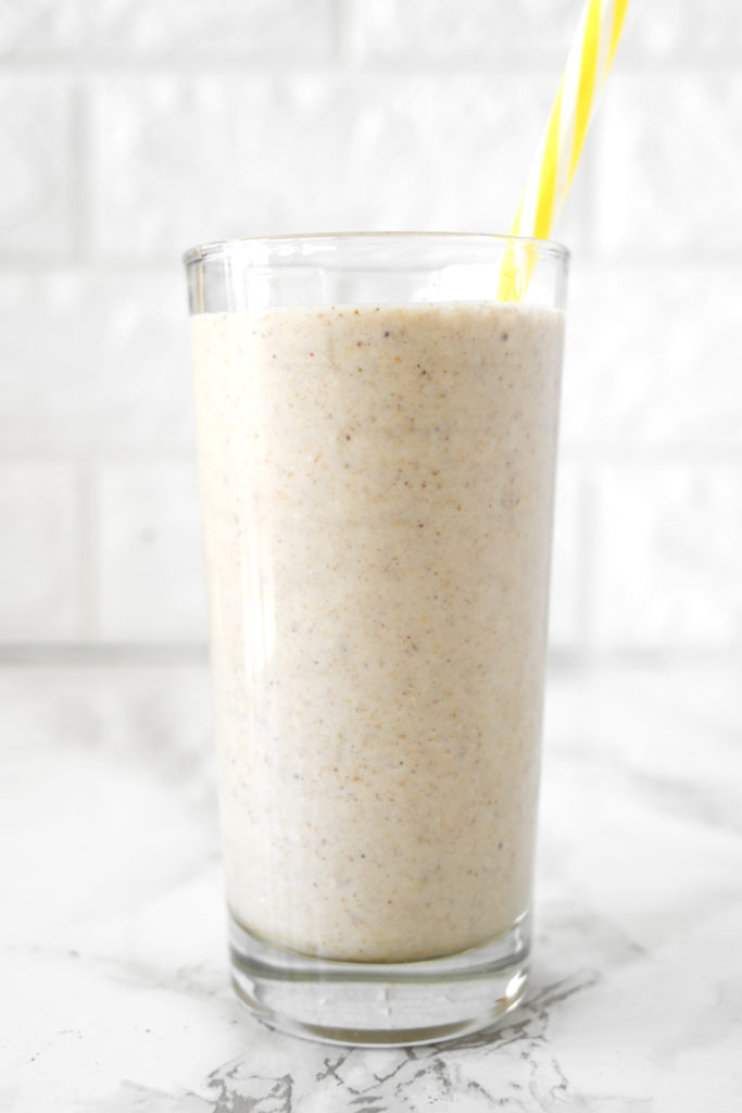 Banana Smoothie with Almond Milk in a glass on a white marble counter with a yellow straw