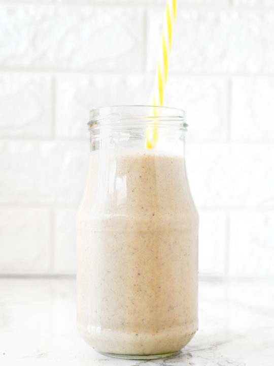 Banana Smoothie with Oat Milk in a glass with a yellow straw on a white marble counter